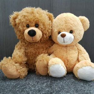 Two brown teddy bears sitting together on a gray surface.