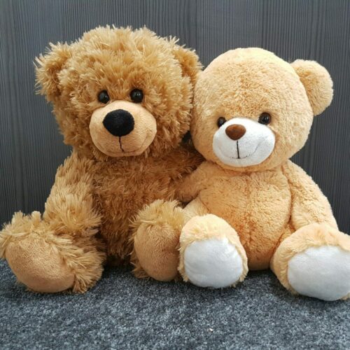 Two brown teddy bears sitting together on a gray surface.