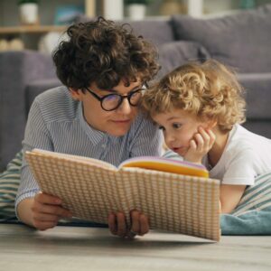 a woman and a child laying on the floor reading a book